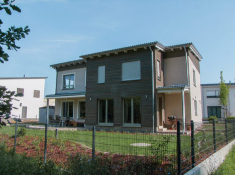 Dieses moderne zweistöckige Haus in Dresden besticht durch eine beeindruckende Kombination aus dunklem Holz und hellem Stuck, die durch große Fenster und einen eingezäunten Garten noch verstärkt wird. Die sonnige Terrasse ist mit Gartenmöbeln und einem Grill ausgestattet und eignet sich ideal für Hausbau-Enthusiasten, um den klaren Himmel zu genießen.