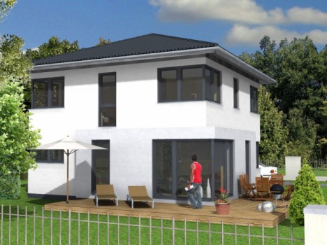 Ein modernes zweistöckiges weißes Haus mit großen Fenstern und einem dunklen Dach in Dresden. Der Hinterhof verfügt über eine Holzterrasse mit einer Person in einem roten Hemd, Liegestühlen, einem Sonnenschirm, einem Esstisch und Topfpflanzen, umgeben von üppigem Grün und einem Metallzaun. Perfekt für alle, die Massivhausbau Dresden erkunden möchten.
