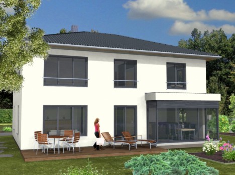 Ein modernes zweistöckiges Massivhaus in Dresden mit großen Fenstern und einer Terrasse. Eine Person steht auf der Holzterrasse, die mit einem Tisch, Stühlen und Liegen ausgestattet ist. Das Haus ist von Grün umgeben und der Himmel ist teilweise bewölkt.
