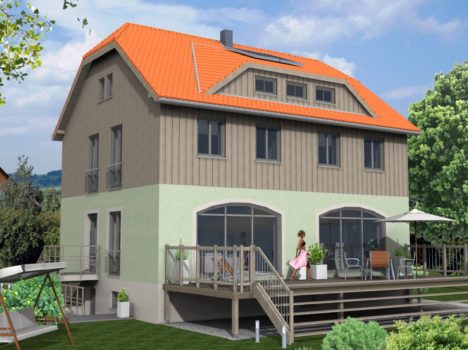 Ein zweistöckiges Haus mit rotem Dach und hellgrüner und brauner Außenfassade ist ein Beweis für exquisiten Hausbau in Dresden. Es verfügt über große Fenster und eine geräumige Holzterrasse mit Gartenmöbeln. Eine Person entspannt sich auf der Terrasse, umgeben von üppigem Grün unter einem teilweise bewölkten Himmel.